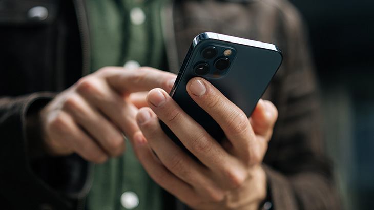 Telefon w dłoni mężczyzny, który palcem drugiej dłoni pracuje na ekranie.