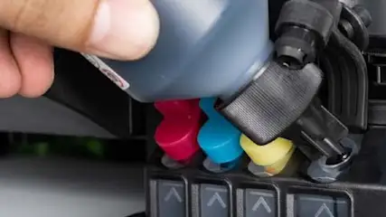 Osoba dolewa czarny tusz do drukarki z kolorowymi wkładami: czerwonym, niebieskim i żółtym.