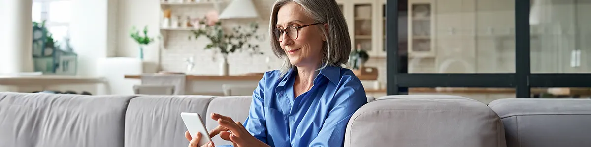 Starsza kobieta siedzi na kanapie i konfiguruje swój telefon.