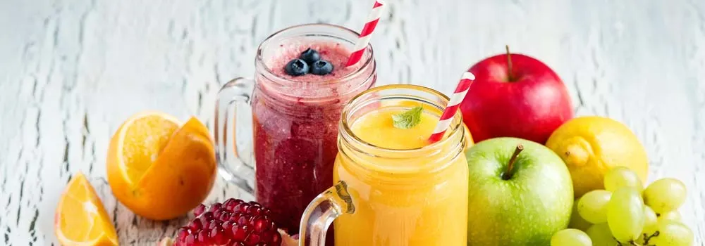 Dwa słoiki z koktajlami obok owoców: pomarańcze, jabłka, winogrona, granat i cytryna na białym, drewnianym tle.