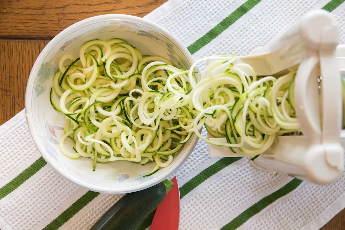 Des courgettes sont transformées en nouilles à l'aide d'un coupe-spirale et placées dans un bol.