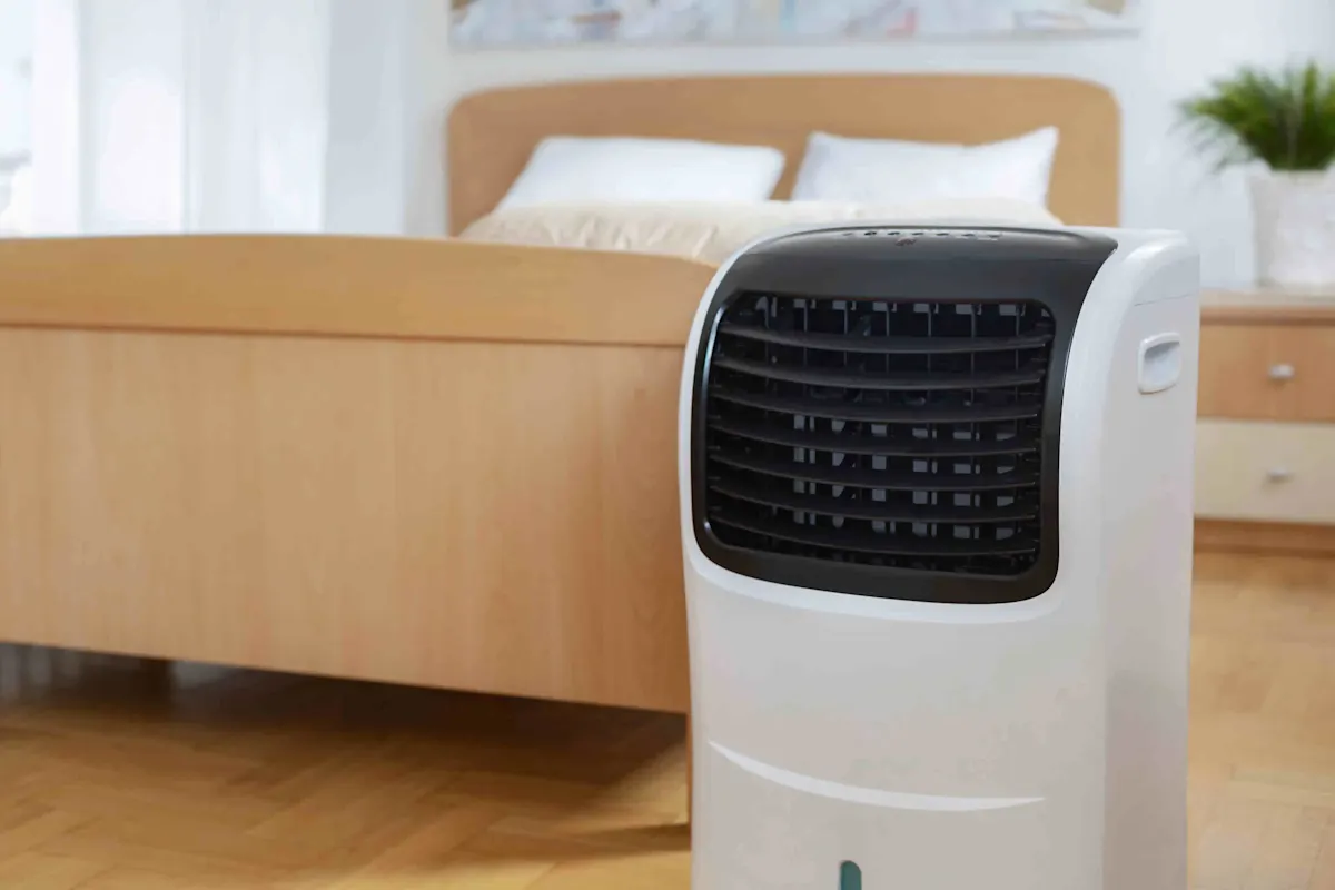 Un refroidisseur d'air mobile se trouve dans une chambre à coucher près d'un lit.