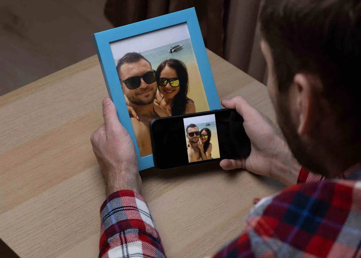 Un homme tient dans la main gauche un cadre photo numérique affichant la photo d’un couple. Dans la main droite, il tient un smartphone sur lequel on voit la même image.