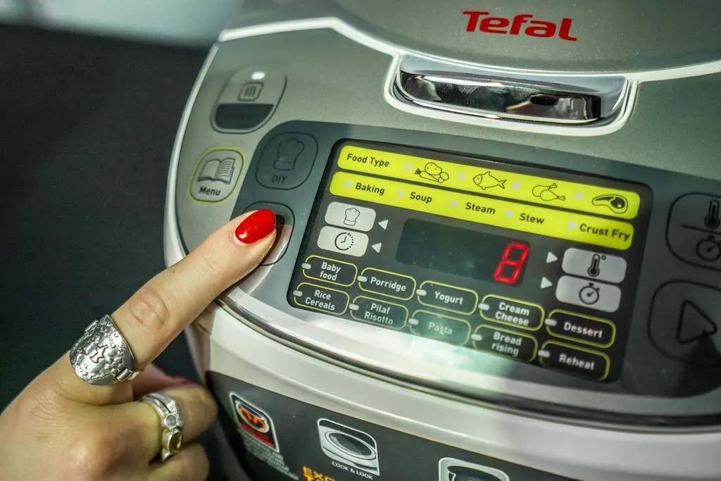 Una mano seleziona un programma di cottura sul pannello di controllo di un multicooker Tefal. 