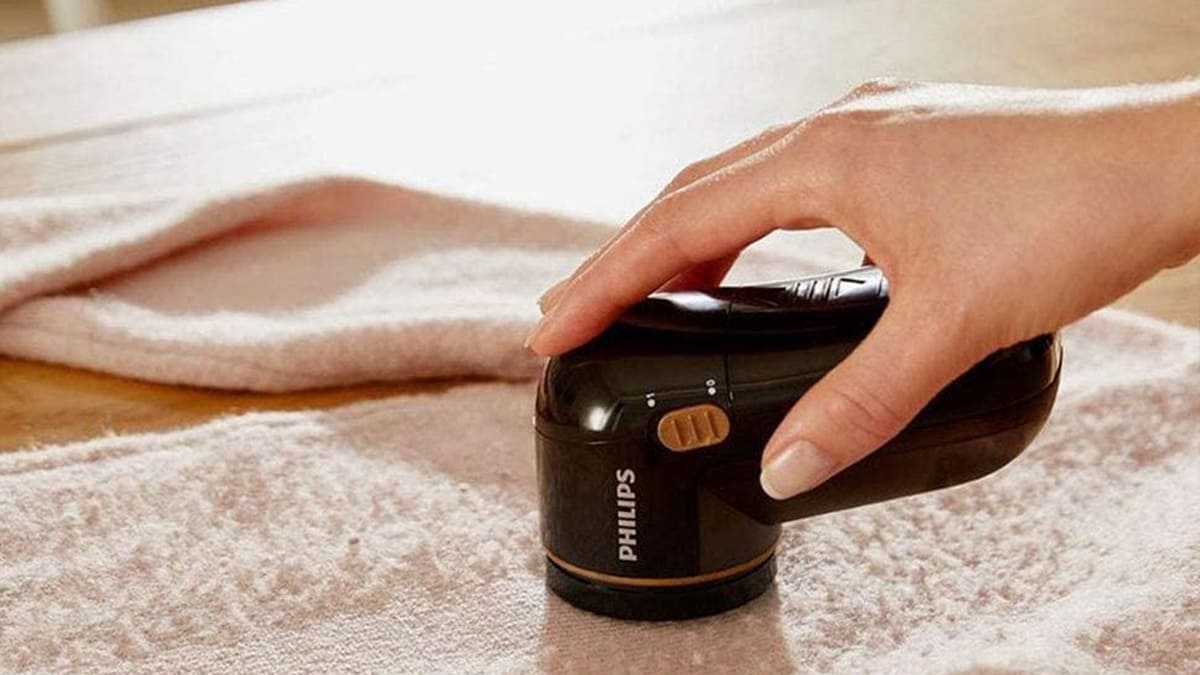 Una mano tiene un levapelucchi nero su un panno rosa chiaro. Il dispositivo ha il marchio Philips.