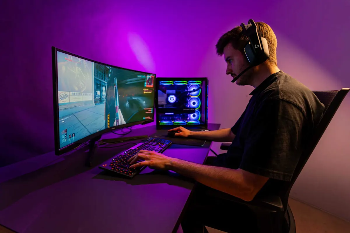 Un giovane uomo è seduto a una scrivania e gioca a un videogioco sul suo monitor.  
