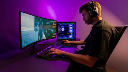 Ein junger Mann sitzt an einem Schreibtisch und spielt ein Computerspiel auf seinem Monitor.