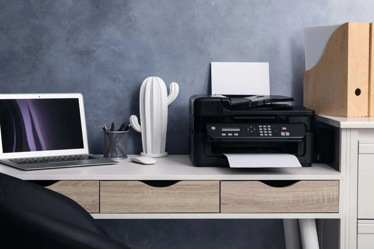 Schwarzer Multifunktionsdrucker auf einem Schreibtisch neben einem Laptop im Homeoffice.