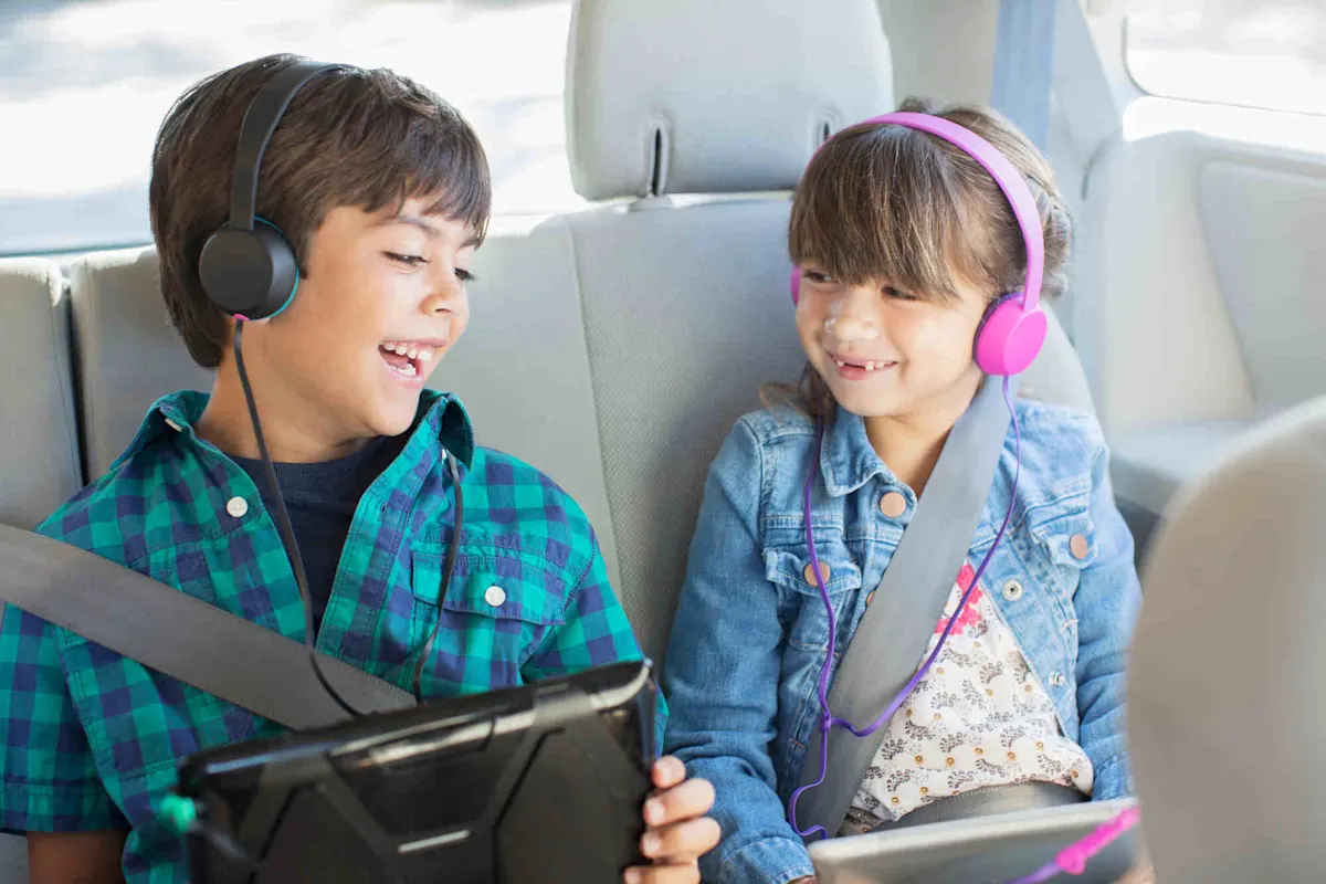 Due bambini ridono sul sedile posteriore di un’auto, con le cuffie e i lettori DVD portatili appoggiati sulle ginocchia.