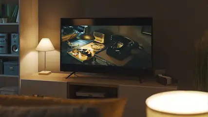 Ein Wohnzimmer mit einem Fernseher, der ein Schreibtischszenario mit einem altmodischen Telefon anzeigt, neben einem Regal und einer Lampe.
