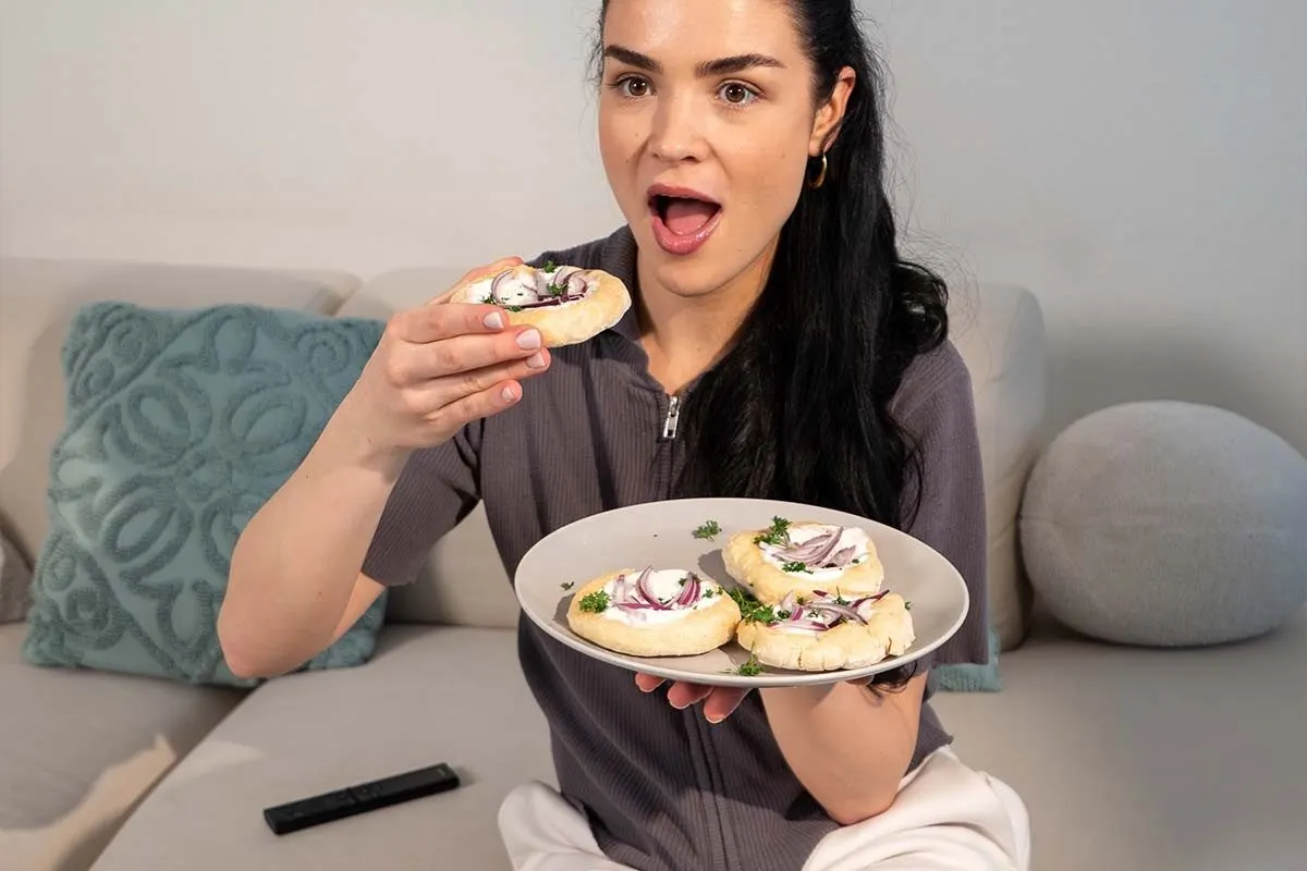 Une femme assise sur le canapé tient une assiette avec des petits pains garnis préparés à l’Airfryer. 