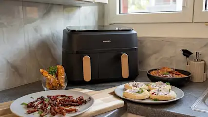 Airfryer Philips con due cestelli su un piano di lavoro in cucina, circondato da diversi finger food.