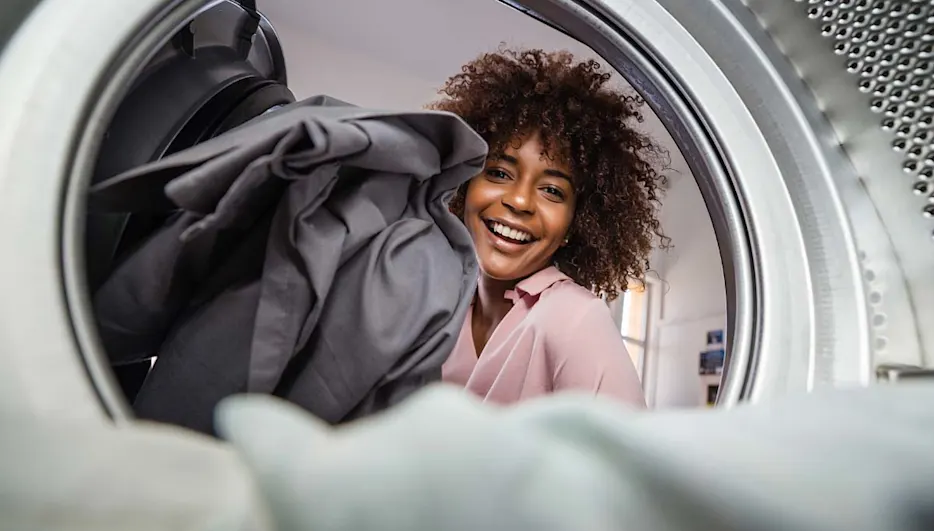 Femme souriante chargeant un sèche-linge avec du linge sombre