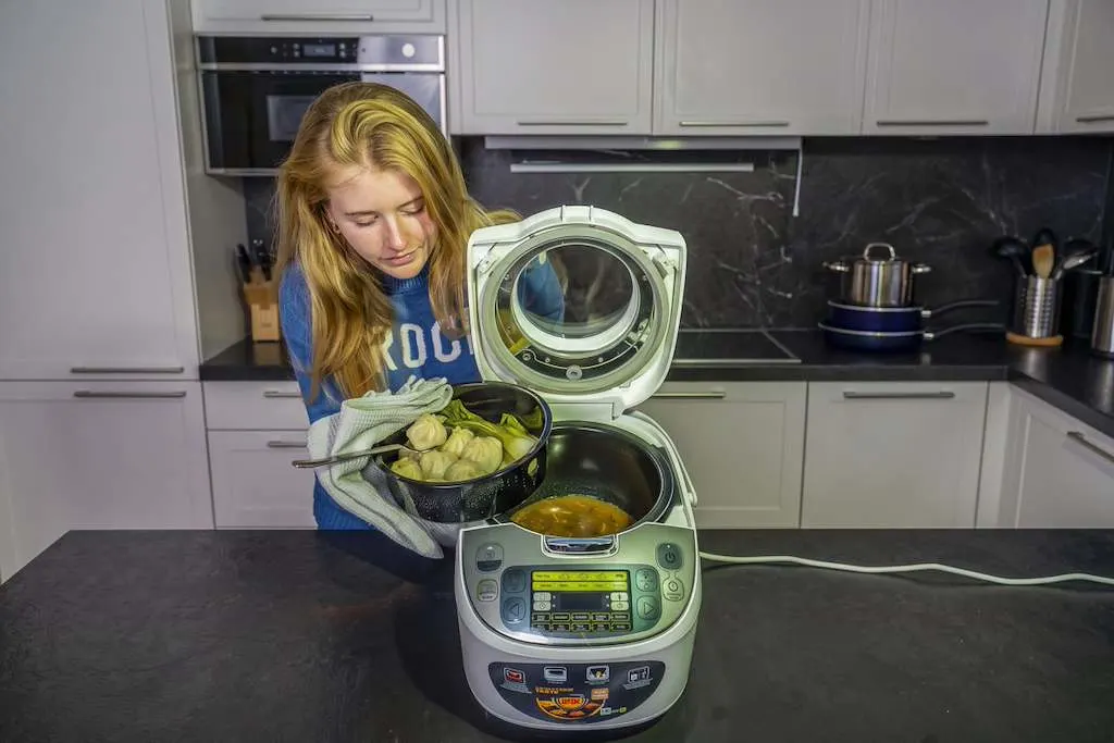 Eine Frau hebt den Dampfgareinsatz mit Momos und Pak Choi aus einem geöffneten Tefal Multicooker.