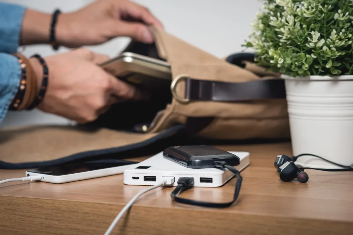 Une powerbank posée sur une table recharge plusieurs appareils à côté d’un sac et d’écouteurs.