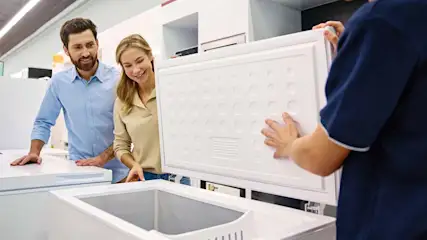 Un conseiller montre à un couple un congélateur coffre ouvert en magasin.