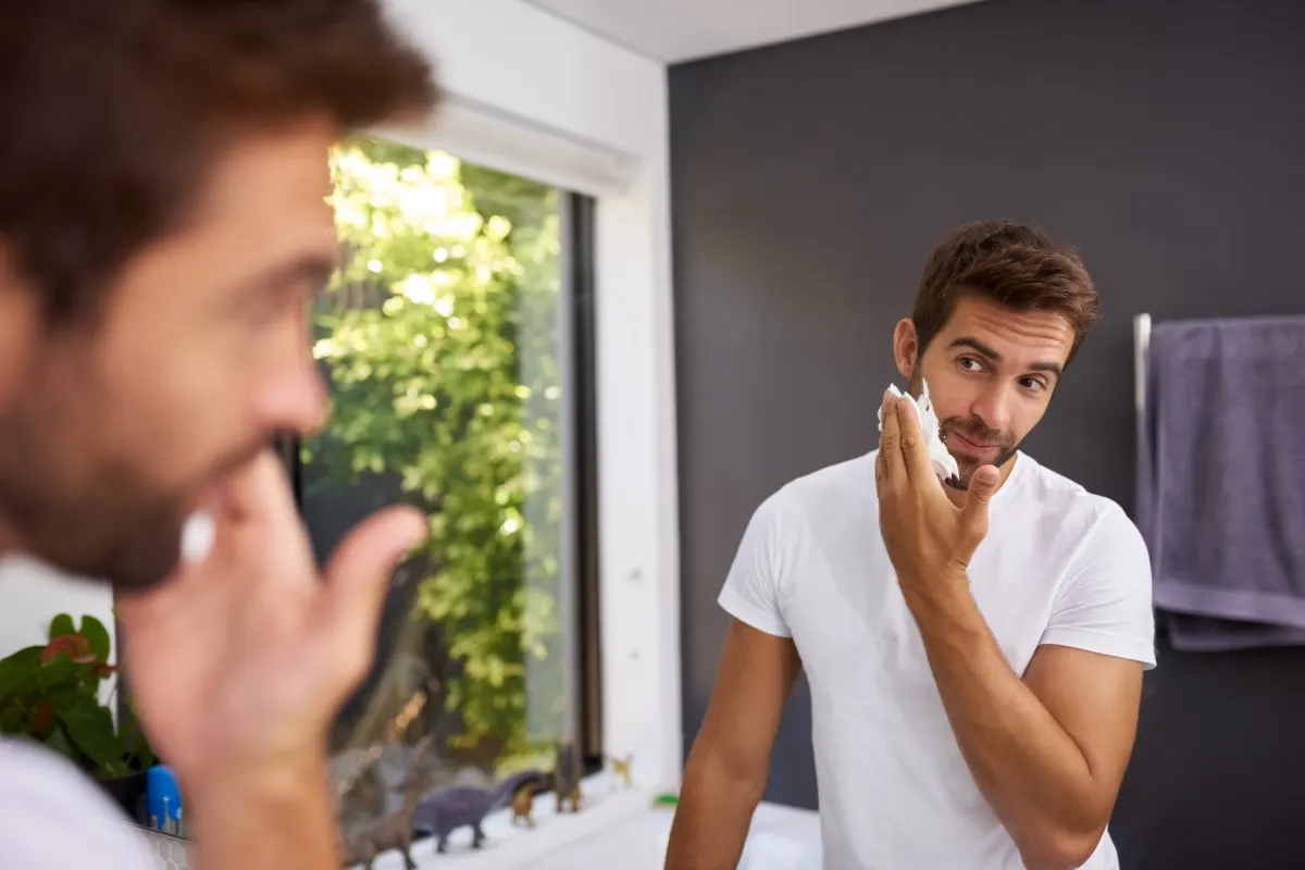 Mann trägt vor dem Badezimmer Rasierschaum auf sein Gesicht auf.