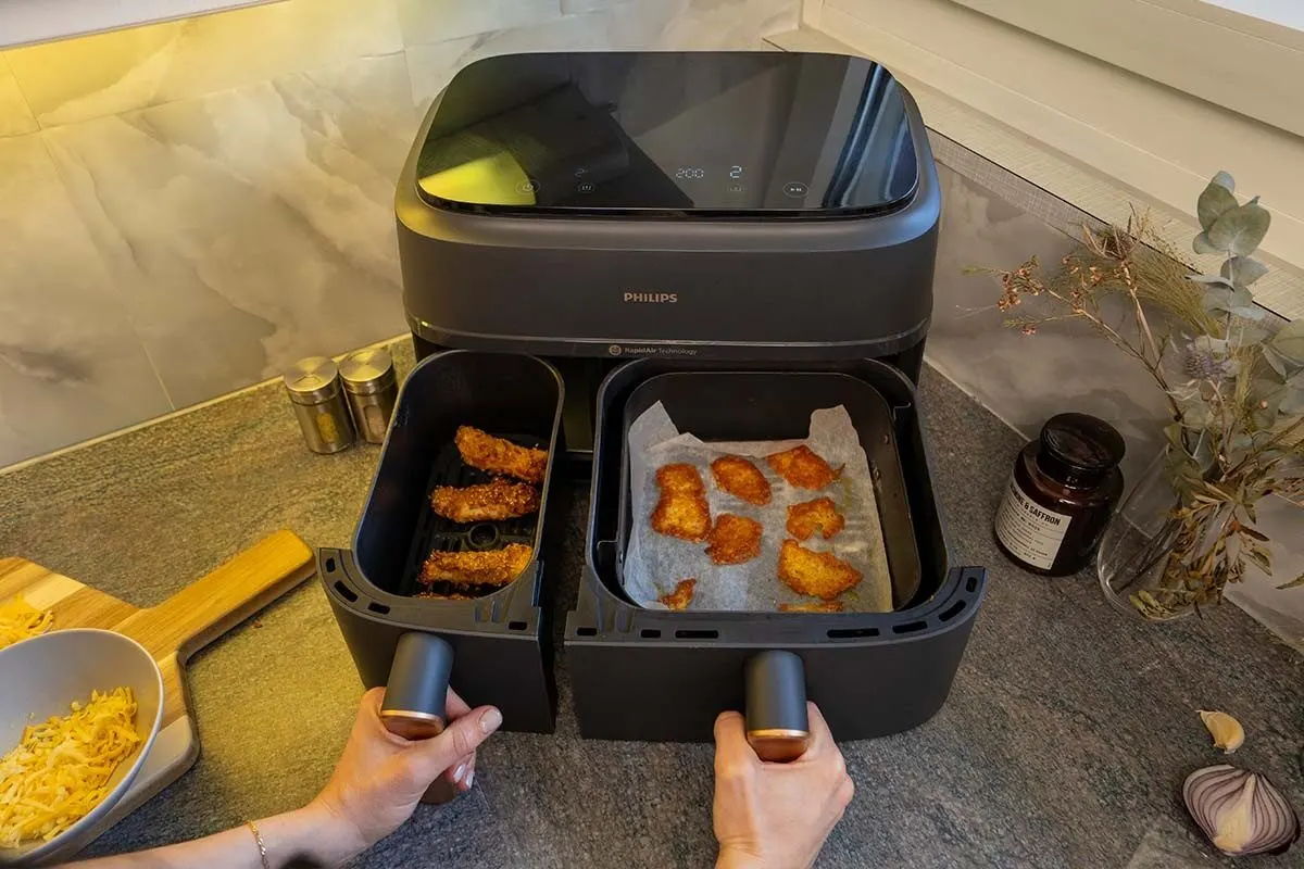 Airfryer Philips aperto con due cestelli contenenti pezzi di finger food impanati e cotti. 