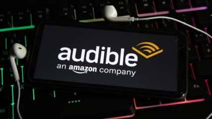 Uno smartphone poggia su una tastiera illuminata RGB con cuffie in-ear e visualizza il logo Audible.