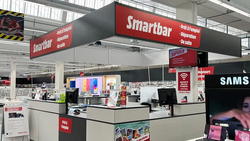 Magasin d'électronique avec stand Smartbar, affichant des téléphones et des services de réparation sur des comptoirs blancs.