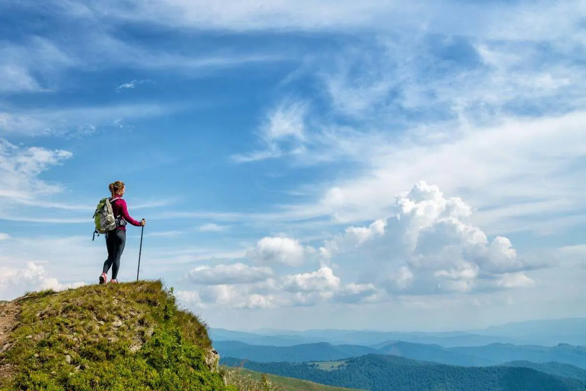 Wanderin steht auf einem Hügel und blickt in den bewölkten Himmel. 