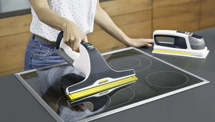 Una persona pulisce un piano cottura nero con un pulitore a vapore portatile bianco e giallo. Un altro pulitore è sul bancone.