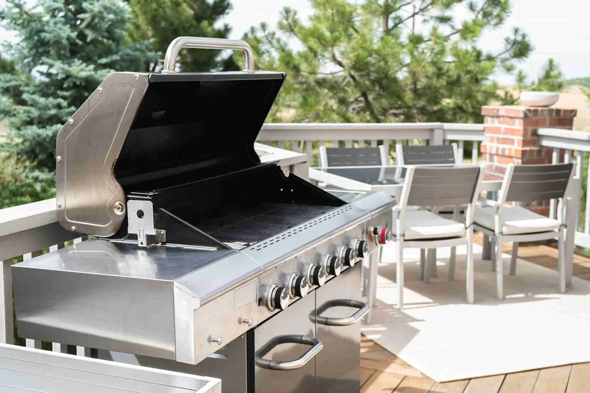 Barbecue a gas aperto in acciaio inox su una terrazza soleggiata, accanto a un tavolo da pranzo con più sedie. 