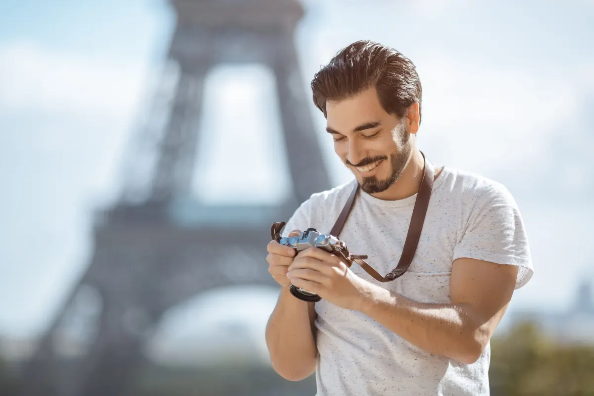 Un uomo guarda foto su una fotocamera, sullo sfondo si intravede sfocata la Torre Eiffel.