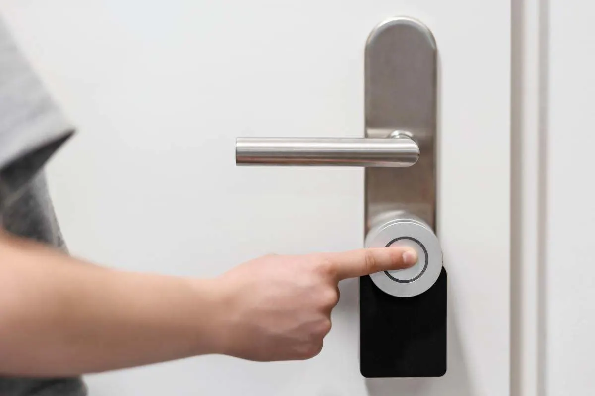 Une personne touche du doigt une serrure connectée fixée sur une porte pour la déverrouiller. 