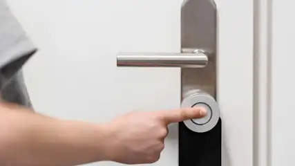 Una persona tocca con il dito una serratura smart montata su una porta per sbloccarla.