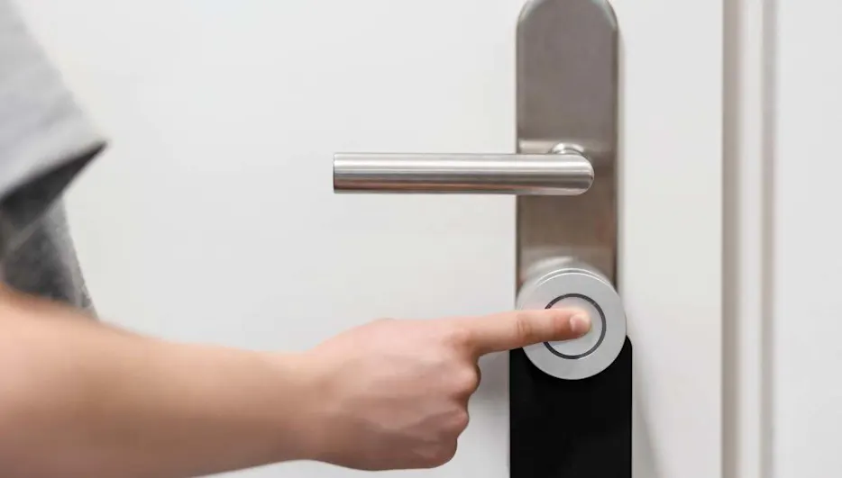 Una persona tocca con il dito una serratura smart montata su una porta per sbloccarla.