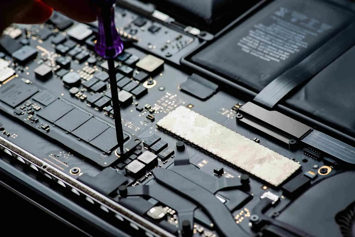 La main d’un technicien tient un tournevis au-dessus d’une SSD endommagée sur un circuit imprimé. 