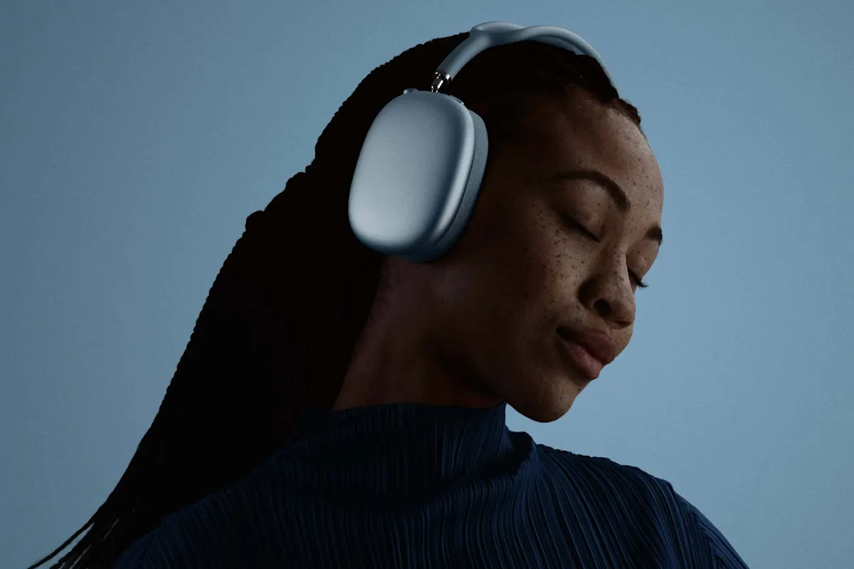 Person mit geschlossenen Augen trägt die Apple AirPods Max 2 in Hellblau vor blauem Hintergrund in stimmungsvoller Lifestyle-Aufnahme.