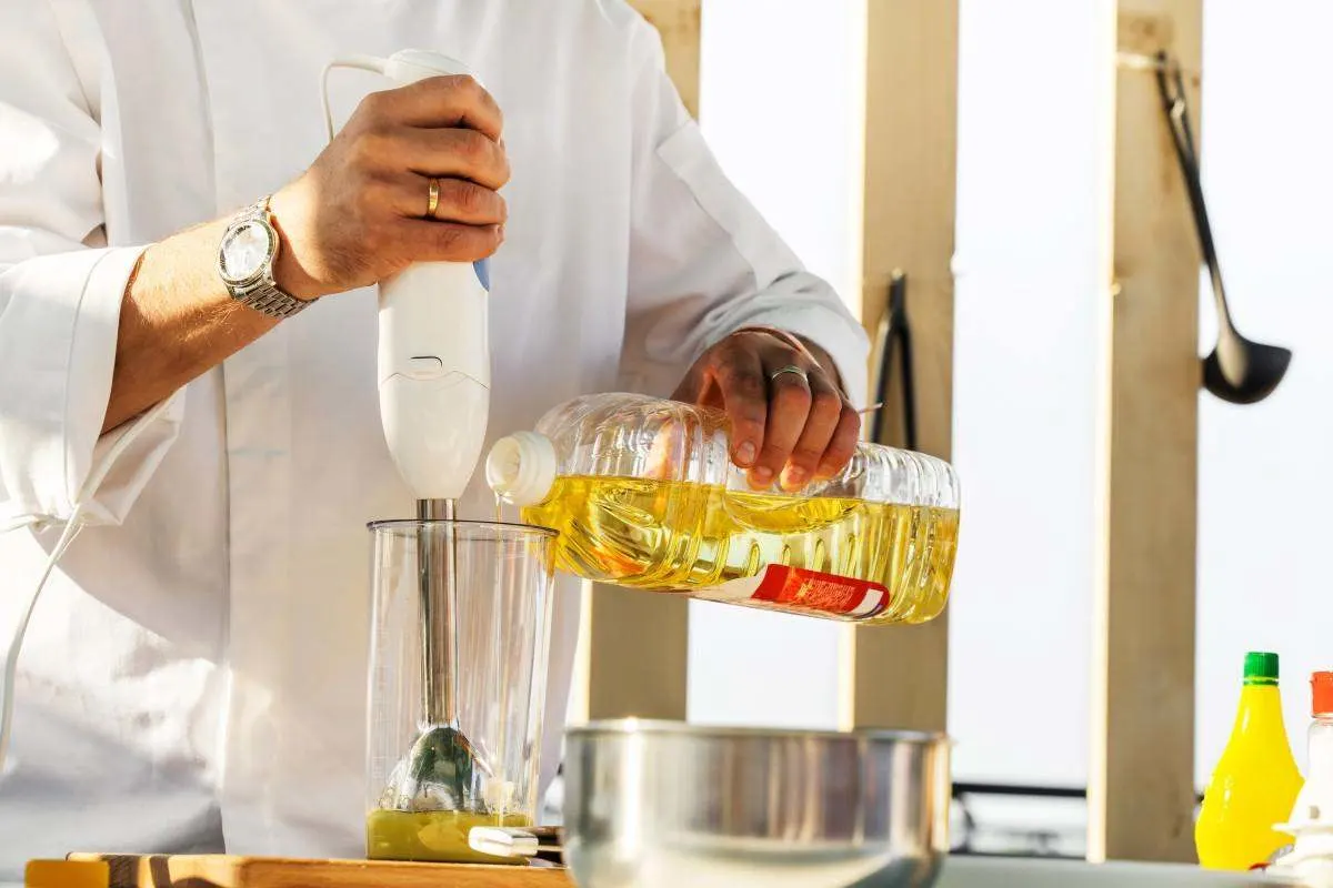 Person giesst Speiseöl in einen Mixbecher und arbeitet mit einem Stabmixer.