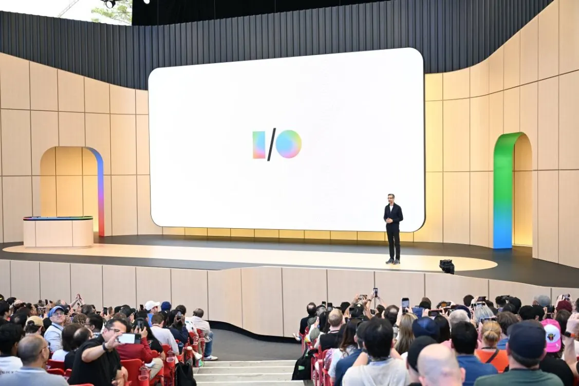 Un orateur se tient devant un grand logo Google I/O sur scène, face au public. 