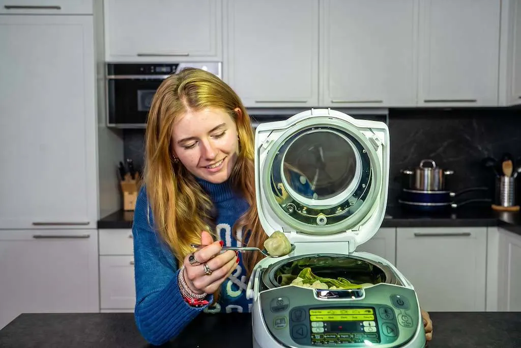 Une femme goûte un momo cuit à la vapeur avec une fourchette dans un multicuiseur Tefal ouvert. 
