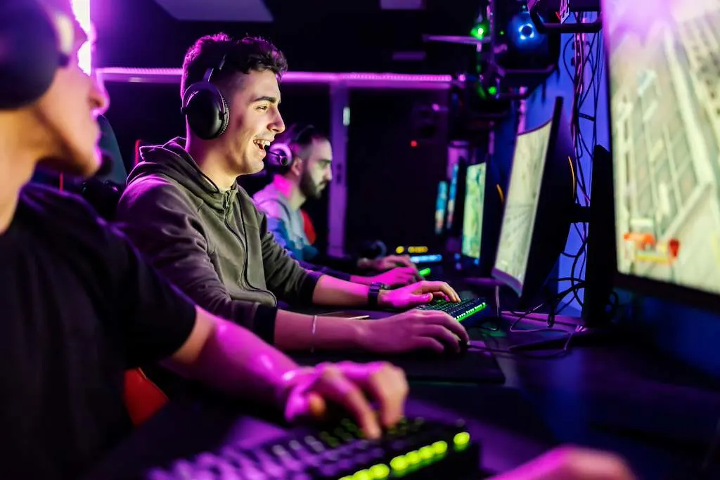 Plusieurs gamers portant des casques jouent sur des PC gaming dans un espace e-sport à l’éclairage sombre. Au premier plan, un jeune homme joue concentré devant son écran.