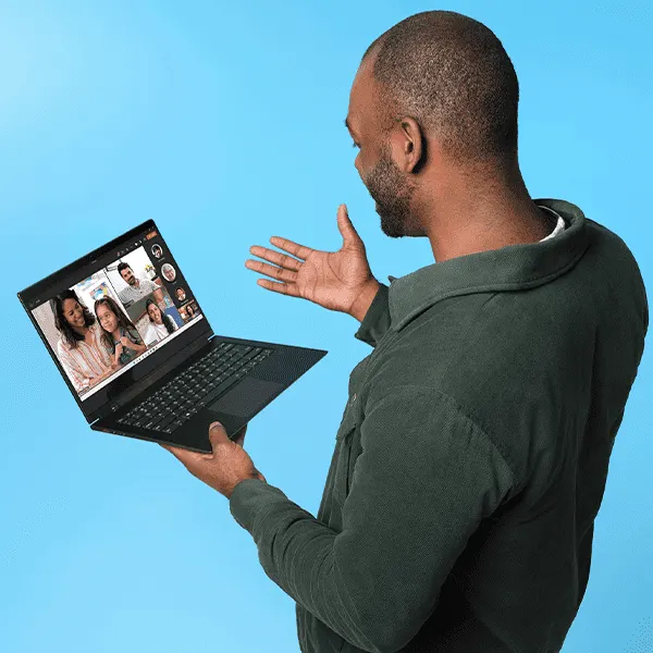 Ein Mann mit einem dunkelgrünen Hemd hält ein schwarzes Windows Notebook  und videotelefoniert gleichzeitig mit mehreren Personen.