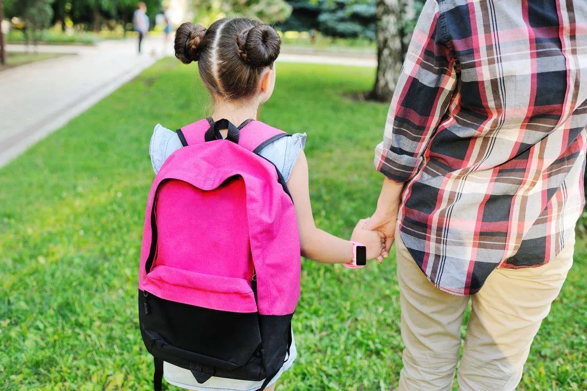 Mädchen mit rosa Smartwatch für Kinder am Handgelenk auf dem Schulweg mit einem Elternteil.