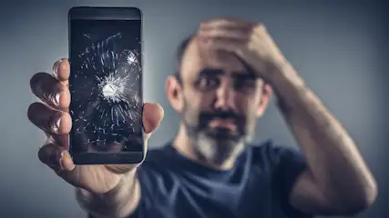 Ein Mann hält verzweifelt ein Handy mit gesprungenen Display in die Kamera
