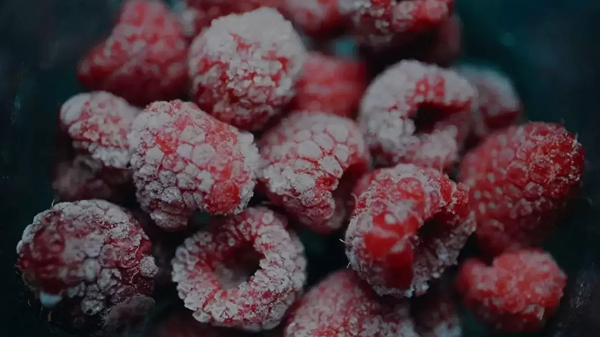 Framboises rouges givrées, formant un amas sur fond sombre. Les fruits présentent une texture granuleuse et des nuances de rouge.