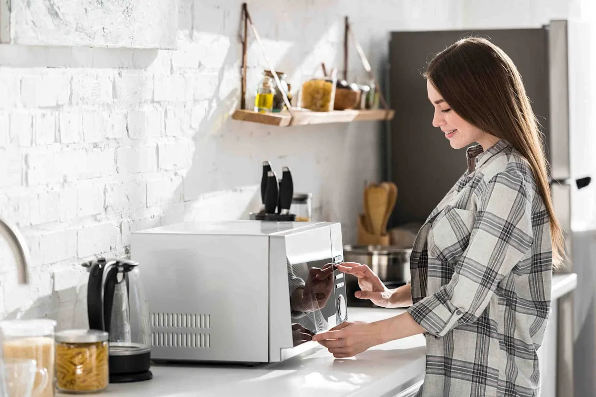 Una giovane donna con una camicia a quadri si trova in cucina e utilizza il pannello touch di un microonde. 