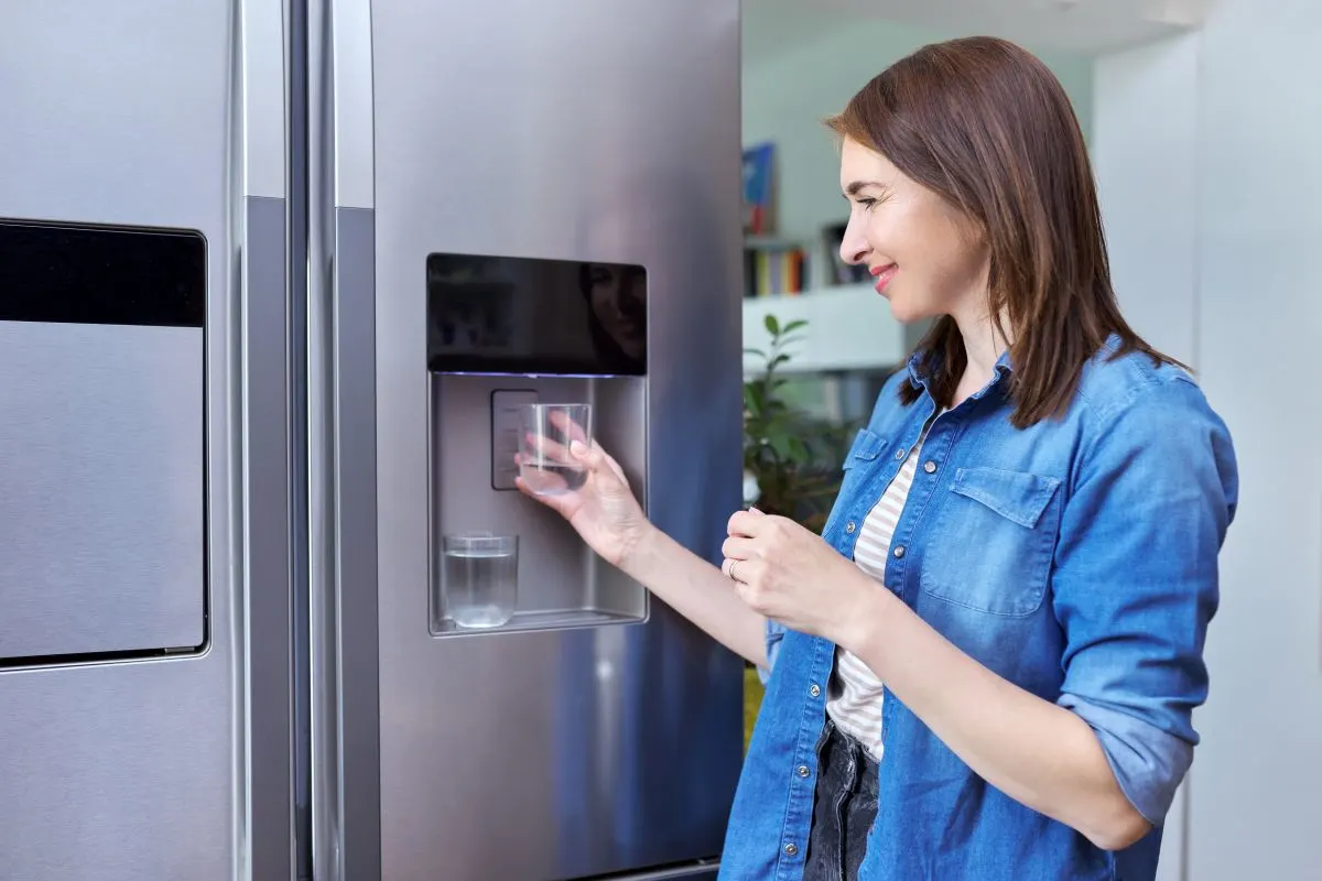 eine Frau füllt bei einem Side-by-Side Kühlschrank ein Glas mit Wasser