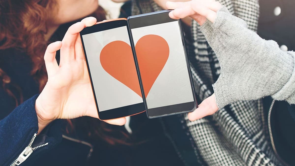 Deux personnes tiennent des téléphones affichant un cœur orange sur fond blanc. Les vêtements sont noirs et à  carreaux.