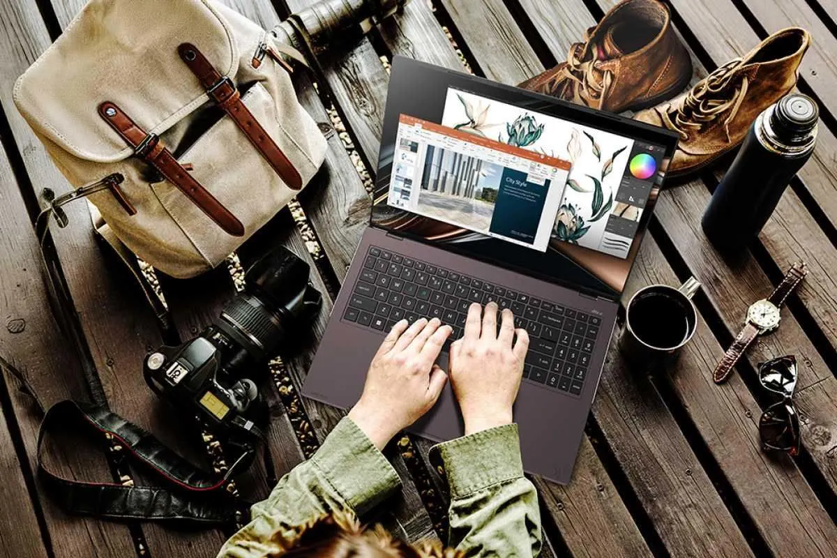 Person arbeitet im Freien an einem Acer Vero 16 Laptop auf einem Holztisch, umgeben von Kamera, Rucksack, Wanderschuhen, Trinkflasche und Kaffee.