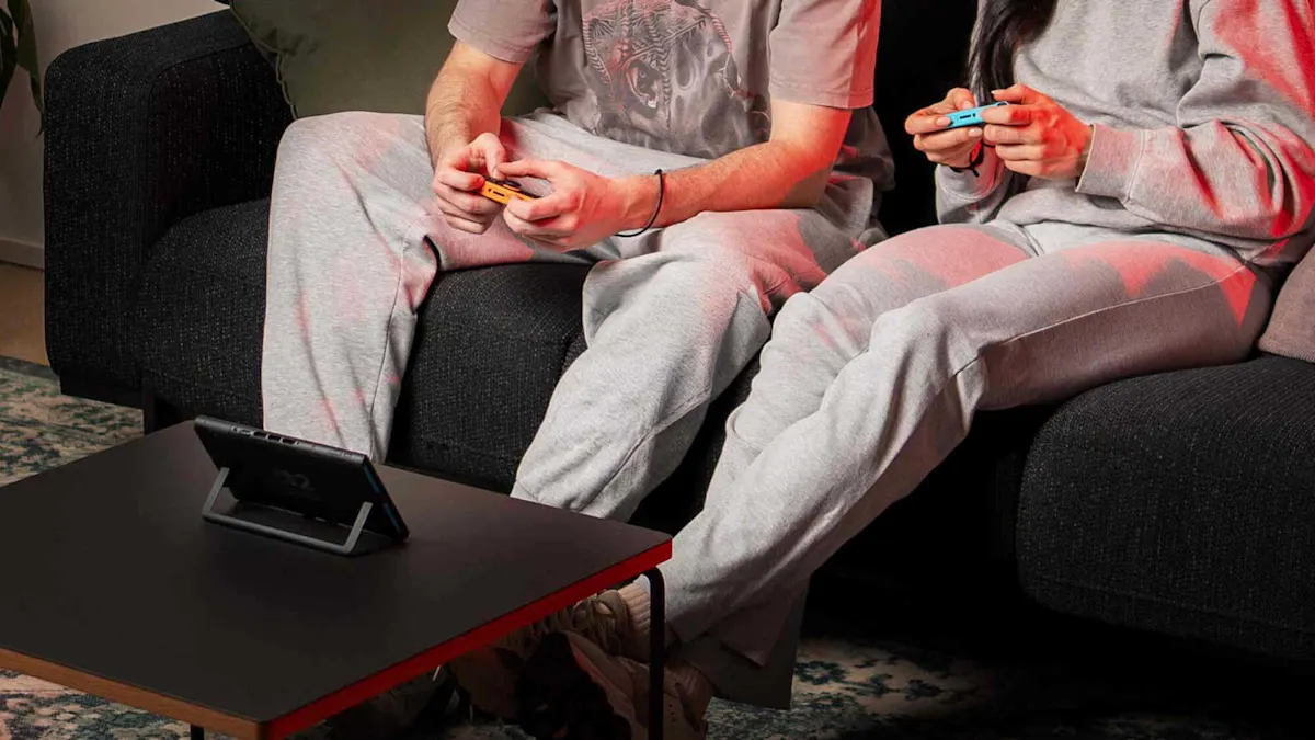 Una Nintendo Switch 2 è posizionata su un tavolo, mentre sullo sfondo due persone giocano insieme. 
