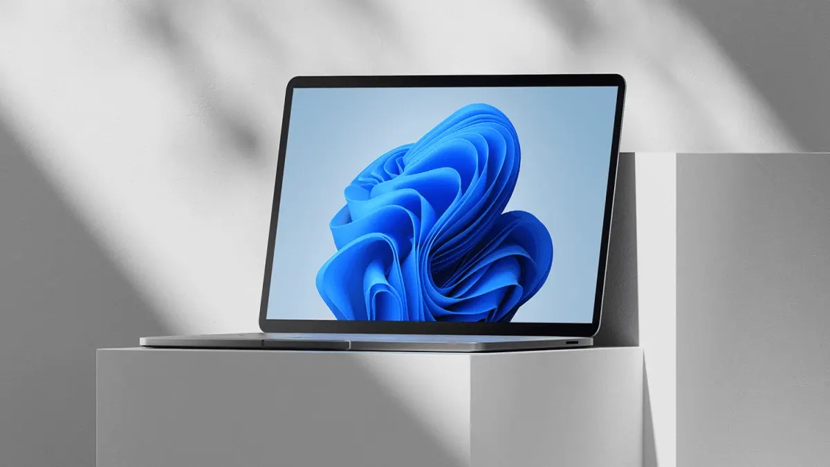 Un computer portatile aperto su un piedistallo bianco mostra uno sfondo blu astratto sullo schermo.