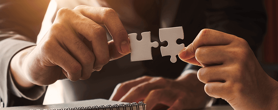Due mani tengono dei pezzi di puzzle bianchi pronti per essere uniti. In primo piano c’è un taccuino.
