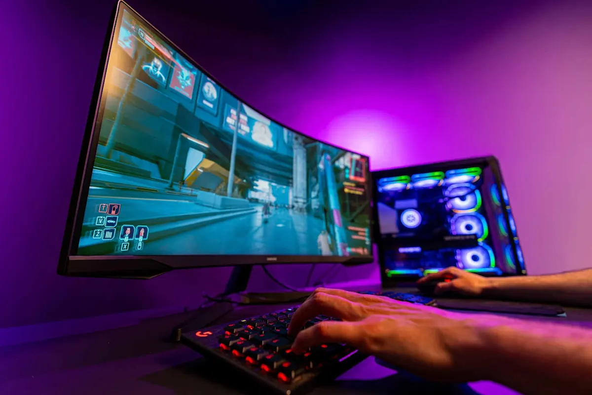 Mano sinistra sulla tastiera, grande monitor da gaming visibile.  