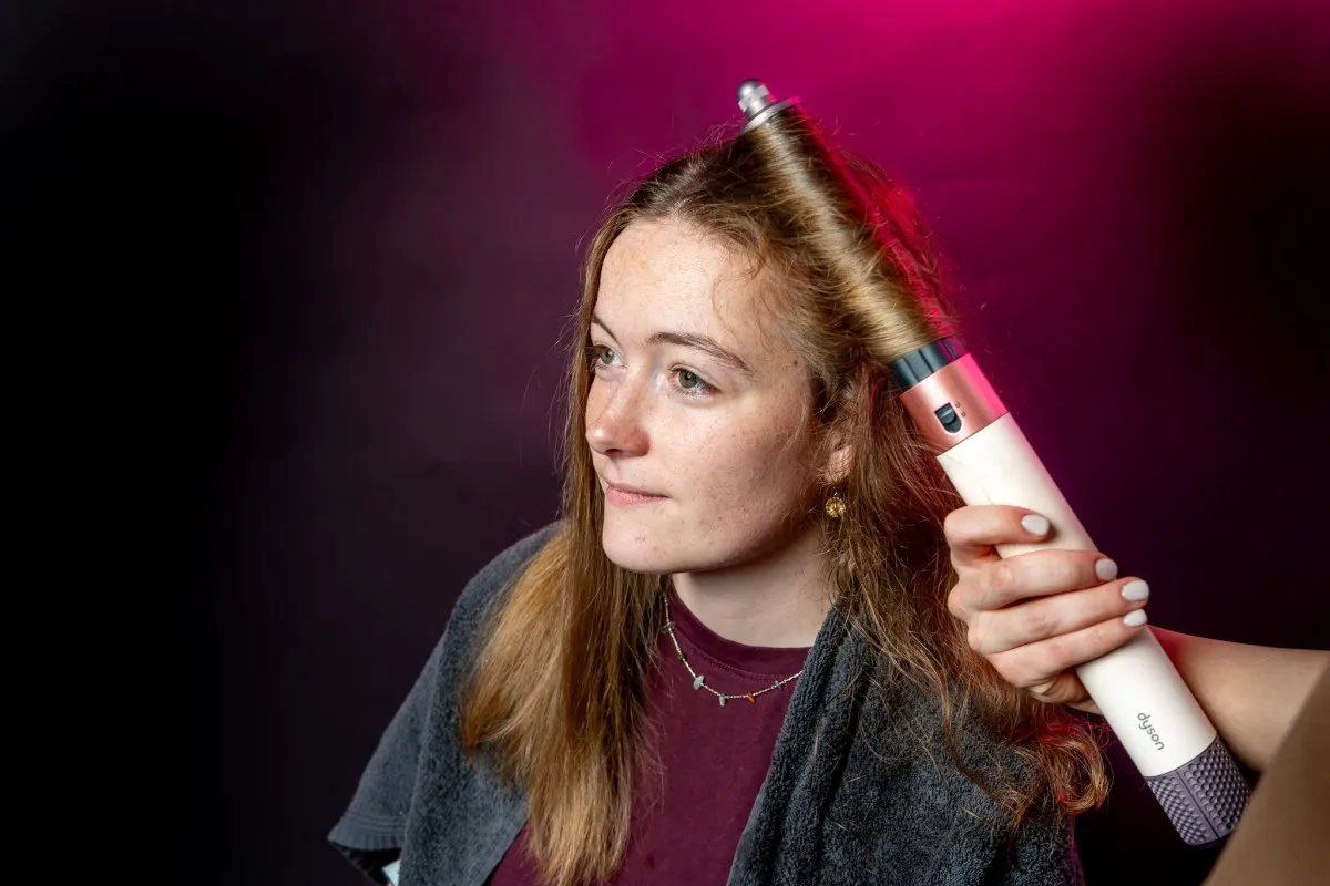Eine Frau stylt ihre Haare mit dem Dyson Airwrap und formt eine Strähne zu einer Welle.